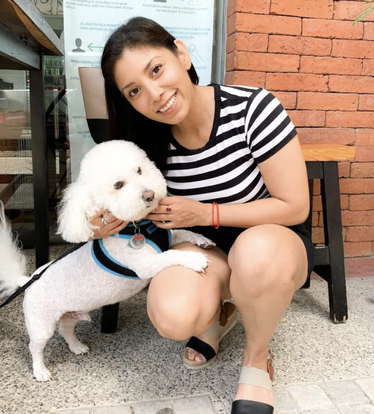 Miriam Siordia, a Realtor Specialist in Luxury Real Estate, kneels next to a white poodle.